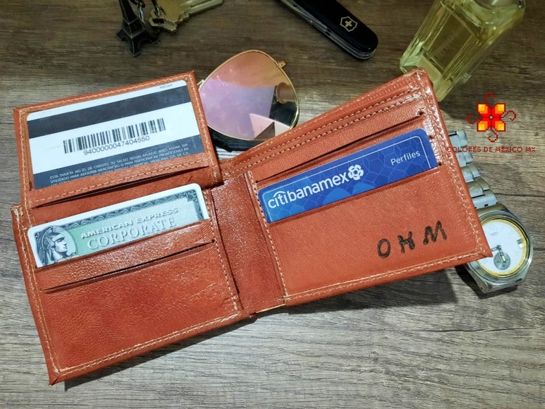 Puede incluir: Una cartera de cuero marr&oacute;n con una ranura para tarjeta de cr&eacute;dito y un portafolios. La cartera tiene una inscripci&oacute;n personalizada que dice "OHM".