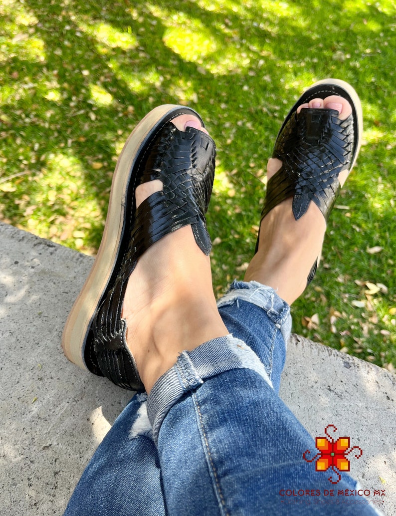 May include: Black leather sandals with woven straps and a platform sole. The sandals are worn by a person wearing blue jeans.