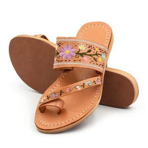 K&ouml;nnte beinhalten: Tanfarbene Ledersandalen mit floralem Stickmuster. Die Sandalen haben eine Zehenschlaufe und einen Kn&ouml;chelriemen.