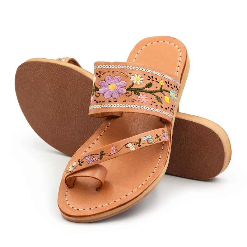 K&ouml;nnte beinhalten: Tanfarbene Ledersandalen mit floralem Stickmuster. Die Sandalen haben eine Zehenschlaufe und einen Kn&ouml;chelriemen.