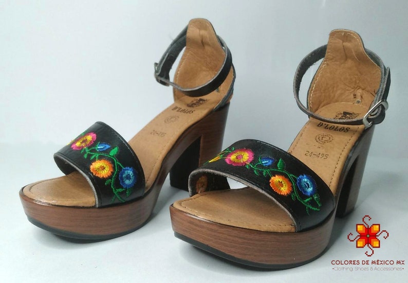 May include: Black leather sandals with a floral embroidery design. The sandals have a wooden platform and a high heel. The brand name "D'ZOLOS" is visible on the sandals.