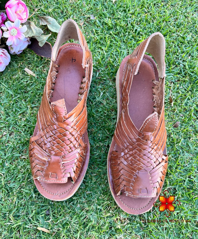 May include: A pair of brown leather sandals with woven straps. The sandals have a simple design and are made of high-quality leather.