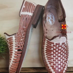 K&ouml;nnte beinhalten: Ein Paar braune Ledersandalen mit gewebtem Muster. Die Sandalen haben einen wei&szlig;en Lederbesatz und eine braune Ledersohle.
