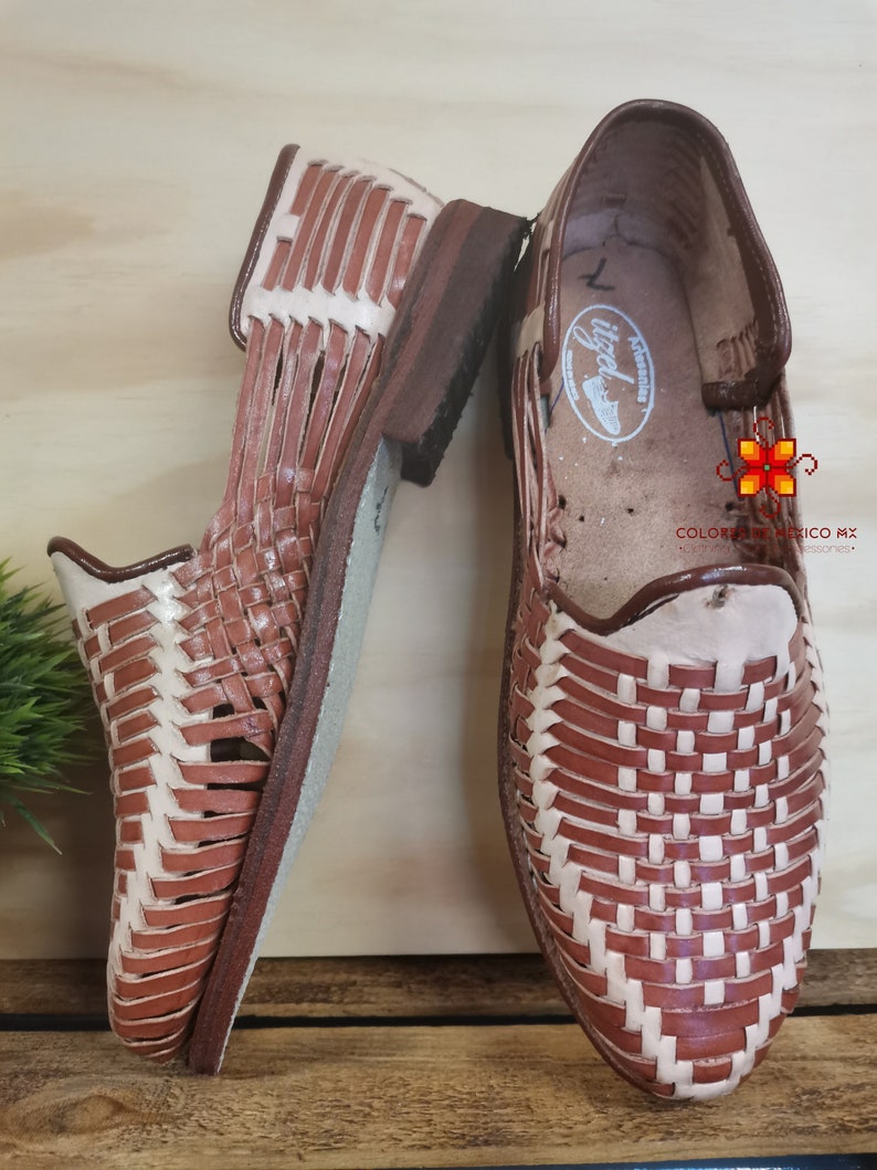 K&ouml;nnte beinhalten: Ein Paar braune Ledersandalen mit gewebtem Muster. Die Sandalen haben einen wei&szlig;en Lederbesatz und eine braune Ledersohle.