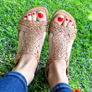 May include: A pair of brown leather sandals with woven straps. The sandals have red nail polish on the toes.