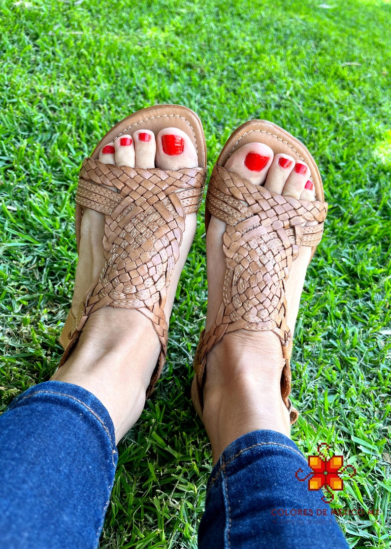May include: A pair of brown leather sandals with woven straps. The sandals have red nail polish on the toes.