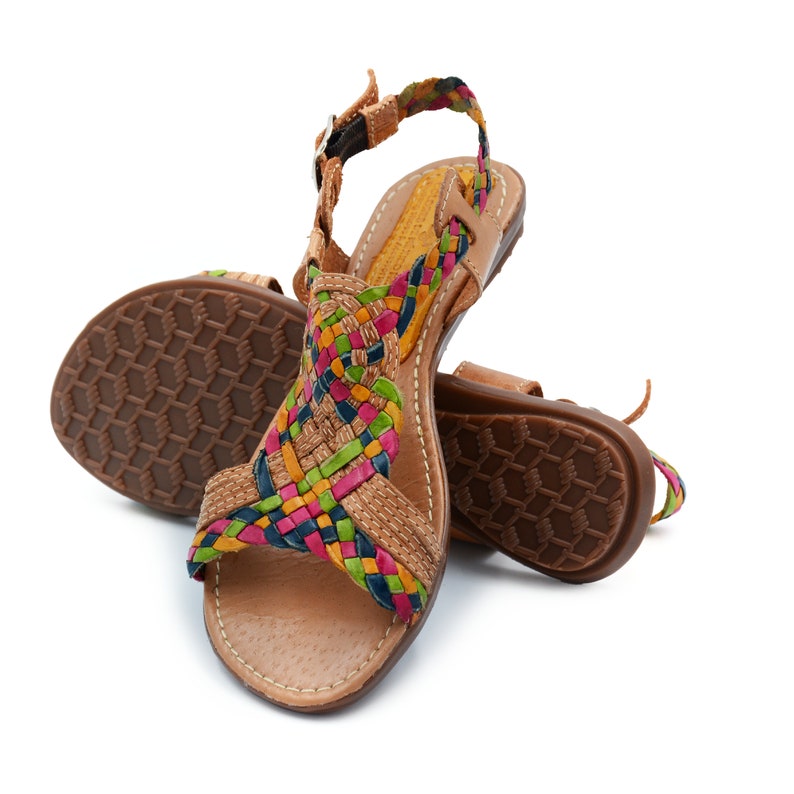 May include: A pair of brown leather sandals with a woven strap design in shades of pink, green, blue, and yellow. The sandals have a closed toe and an ankle strap.