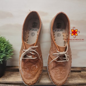 K&ouml;nnte beinhalten: Ein Paar braune Lederschuhe mit aufwendigen Blumenstickereien. Die Schuhe haben Schn&uuml;rsenkel und eine abgerundete Spitze. Der Markenname "D'LOLOS" ist auf der Innenseite jedes Schuhs sichtbar.