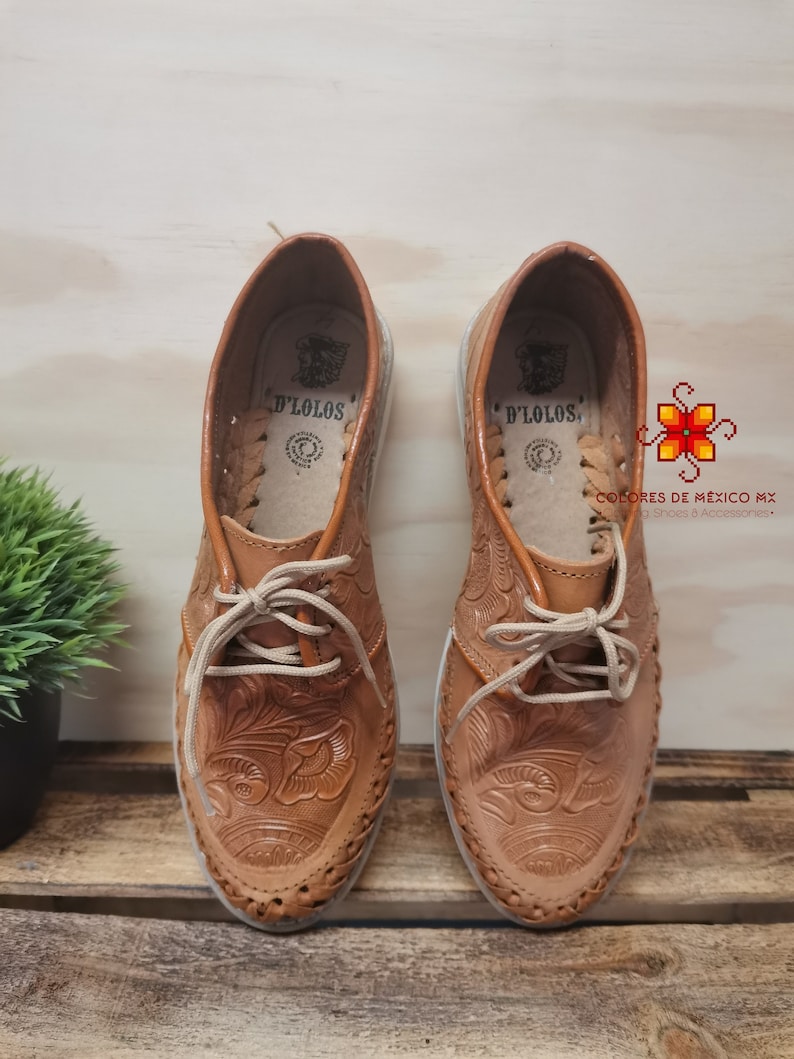 K&ouml;nnte beinhalten: Ein Paar braune Lederschuhe mit aufwendigen Blumenstickereien. Die Schuhe haben Schn&uuml;rsenkel und eine abgerundete Spitze. Der Markenname "D'LOLOS" ist auf der Innenseite jedes Schuhs sichtbar.