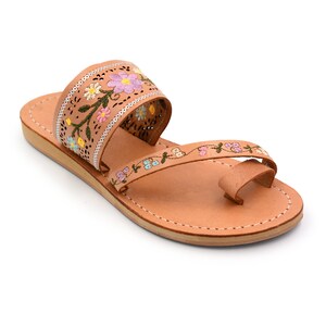 K&ouml;nnte beinhalten: Tannfarbene Ledersandalen mit einem floral bestickten Riemen. Der Riemen ist aus d&uuml;nnem Leder und hat ein zartes Blumenmuster in Rosa, Blau, Gelb und Gr&uuml;n.