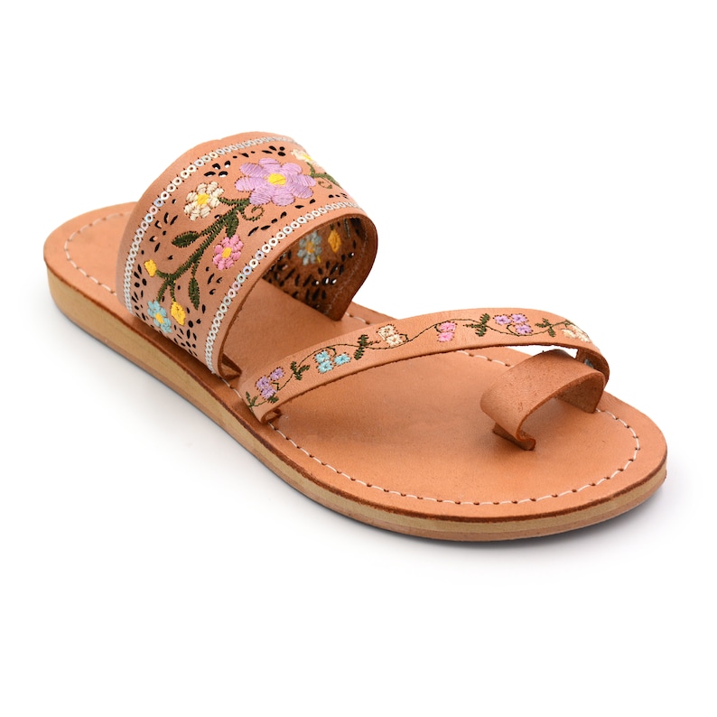 K&ouml;nnte beinhalten: Tannfarbene Ledersandalen mit einem floral bestickten Riemen. Der Riemen ist aus d&uuml;nnem Leder und hat ein zartes Blumenmuster in Rosa, Blau, Gelb und Gr&uuml;n.