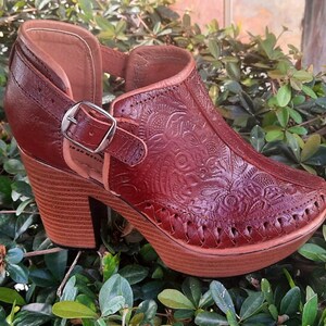 May include: A pair of brown leather heeled shoes with a floral embossed design. The shoes have a buckle closure and a platform heel.