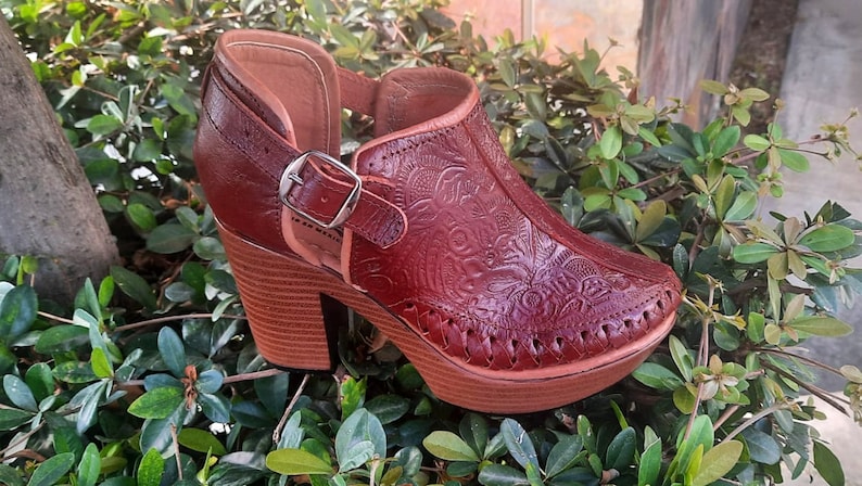 May include: A pair of brown leather heeled shoes with a floral embossed design. The shoes have a buckle closure and a platform heel.