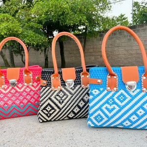 May include: Three woven tote bags with geometric patterns. The bags are pink, black and white, and blue and white. Each bag has a brown leather handle and a silver clasp.