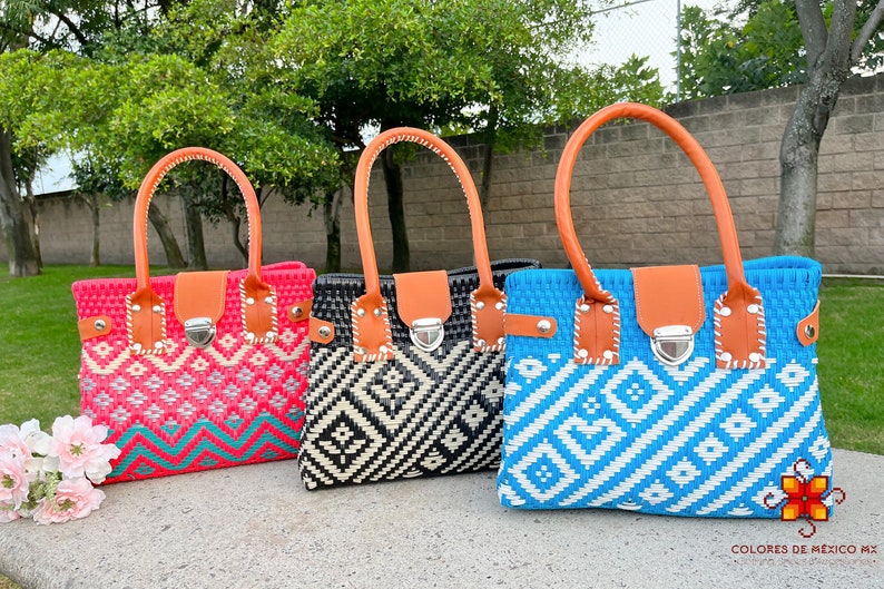 May include: Three woven tote bags with geometric patterns. The bags are pink, black and white, and blue and white. Each bag has a brown leather handle and a silver clasp.