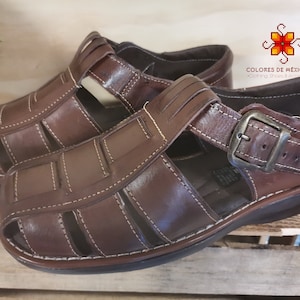 Könnte beinhalten: Braune Ledersandalen mit Schnallenverschluss. Die Sandalen haben ein geflochtenes Design und eine dicke Sohle.