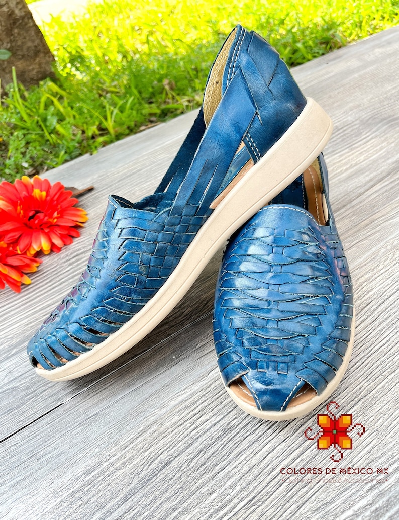 May include: A pair of blue leather sandals with a woven design and a white sole. The sandals have a cutout design and are made of a soft, supple leather.