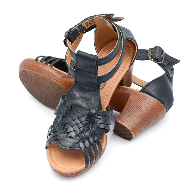 May include: Black leather heeled sandals with a woven design on the front strap and a brown wooden heel.