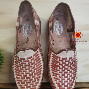 K&ouml;nnte beinhalten: Ein Paar braune Ledersandalen mit gewebtem Design. Die Sandalen haben ein wei&szlig;es Lederfutter und eine braune Ledersohle.
