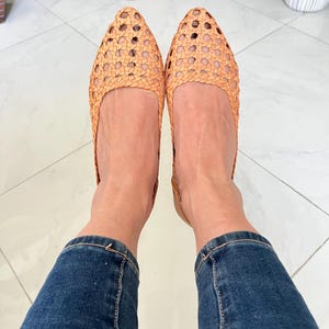 K&ouml;nnte beinhalten: Ein Paar geflochtene Lederschuhe in hellbrauner Farbe. Die Schuhe haben eine spitze Zehenpartie und ein geflochtenes Design. Die Schuhe werden von einer Person getragen, die eine blaue Jeans tr&auml;gt.