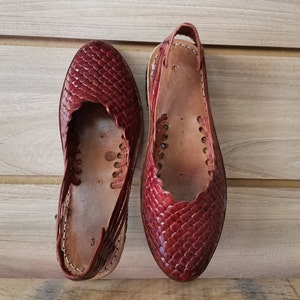 Puede incluir: Un par de sandalias de cuero rojo con un patr&oacute;n tejido. Las sandalias tienen una correa que va alrededor del tobillo y un cierre de hebilla.