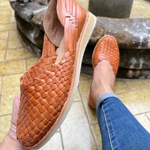 Pu&ograve; includere: Un paio di sandali in pelle marrone con un design intrecciato. I sandali hanno una suola piatta e sono realizzati in pelle morbida e flessibile.