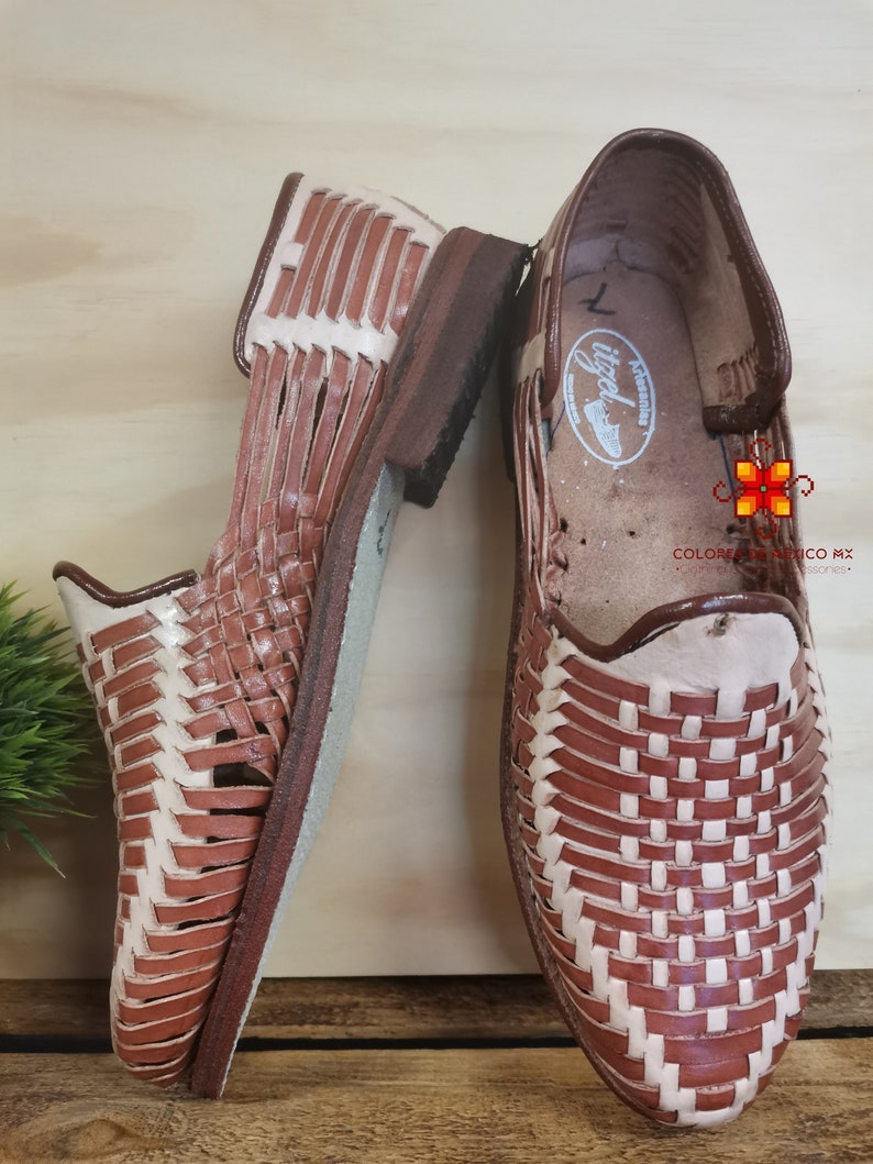 K&ouml;nnte beinhalten: Ein Paar braune Ledersandalen mit gewebtem Design. Die Sandalen haben ein wei&szlig;es Lederfutter und eine braune Ledersohle.
