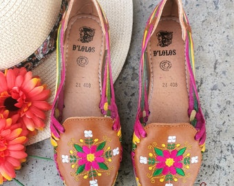 May include: A pair of brown leather sandals with colorful embroidery. The sandals have a pink, green, and yellow striped design and feature a floral pattern on the toe. The sandals are labeled "D'Lolos" and "24 408".