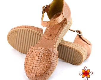 Op de afbeelding: Bruine leren sandalen met een geweven ontwerp en een gespsluiting. De sandalen hebben een wigvormige hak en een rubberen zool.