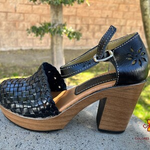 Op de afbeelding: Zwarte leren platform sandalen met een geweven ontwerp en een enkelband. De sandalen hebben een houten hak en een houten platform.