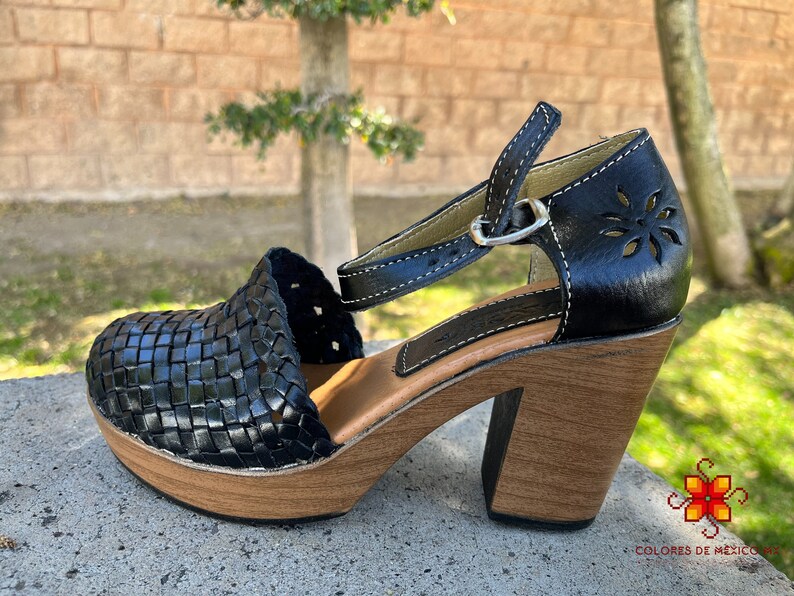 Op de afbeelding: Zwarte leren platform sandalen met een geweven ontwerp en een enkelband. De sandalen hebben een houten hak en een houten platform.