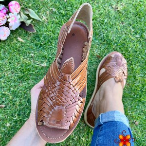 May include: Brown leather sandals with a woven design. The sandals have an open toe and a strap that goes around the ankle.