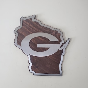 Wall decor cut in a curved map-style outline, with a silver steel emblem over dark brown stained wood and a steel border around the edge. The piece is shown from the front on a light gray background.