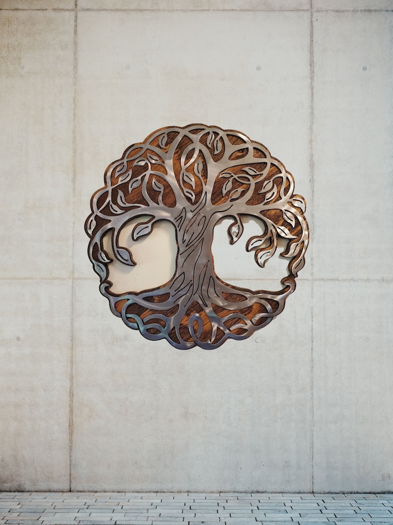 K&ouml;nnte beinhalten: Metall-Wandkunst mit dem Lebensbaum-Motiv. Das Design zeigt eine detaillierte Baum-Silhouette mit filigranen Blatt- und Astmustern. Der Baum ist vor einem h&ouml;lzernen Hintergrund platziert und von einem kreisf&ouml;rmigen Rahmen umgeben. Das Kunstwerk ist an einer Betonwand befestigt.