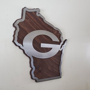 Side-angled view of the map-style wall decor with a silver steel emblem over dark brown wood, showing the layered edge of the piece.