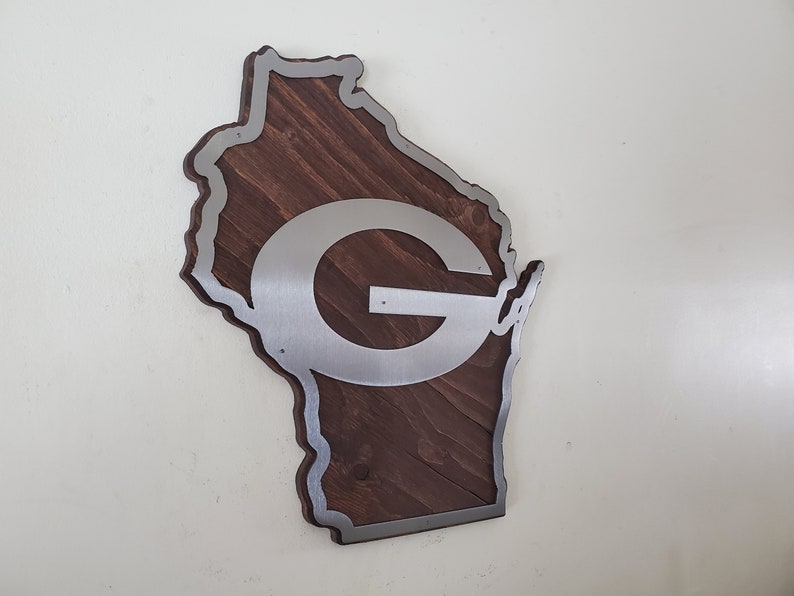 Side-angled view of the map-style wall decor with a silver steel emblem over dark brown wood, showing the layered edge of the piece.