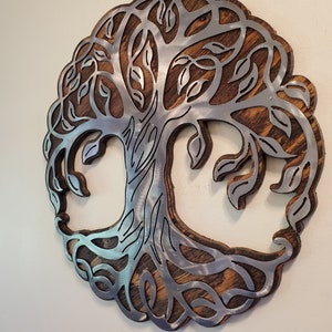 K&ouml;nnte beinhalten: Runde Wanddekoration mit einem Lebensbaum-Design. Der Baum ist aus silberfarbenem Metall gefertigt und vor einem Hintergrund aus gebeiztem Holz angebracht. Die &Auml;ste und Bl&auml;tter des Baumes sind fein detailliert.