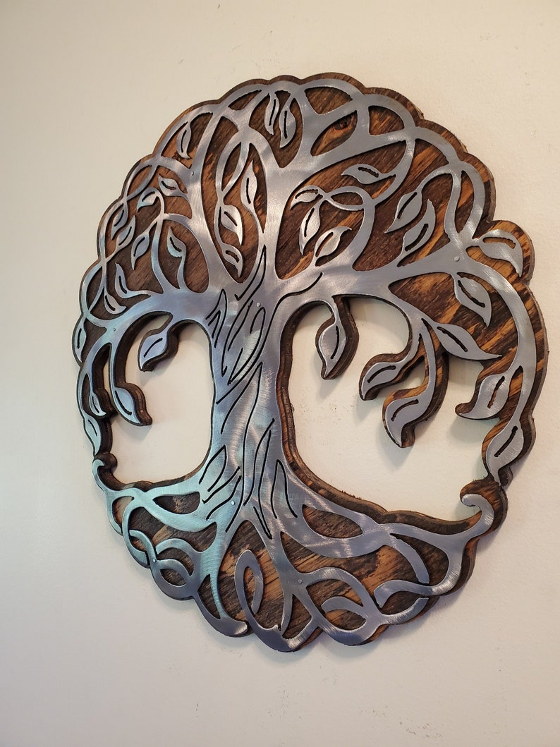 K&ouml;nnte beinhalten: Runde Wanddekoration mit einem Lebensbaum-Design. Der Baum ist aus silberfarbenem Metall gefertigt und vor einem Hintergrund aus gebeiztem Holz angebracht. Die &Auml;ste und Bl&auml;tter des Baumes sind fein detailliert.