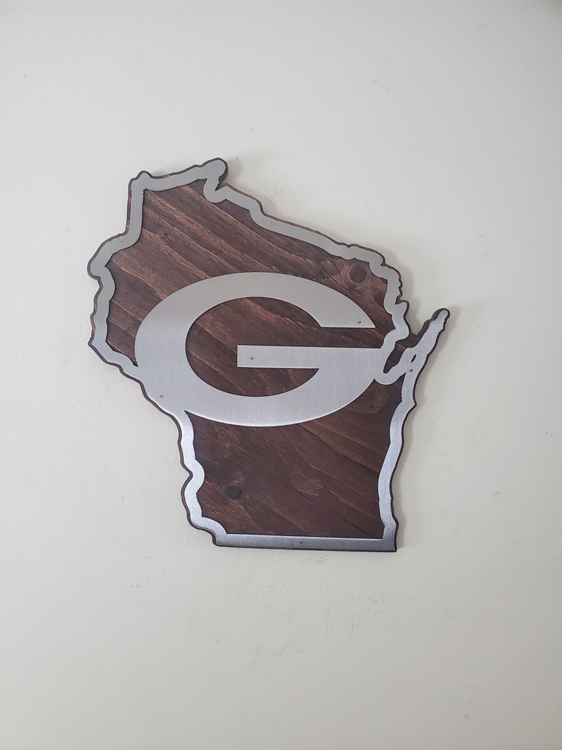 Wall decor cut in a curved map-style outline, with a silver steel emblem over dark brown stained wood and a steel border around the edge. The piece is shown from the front on a light gray background.