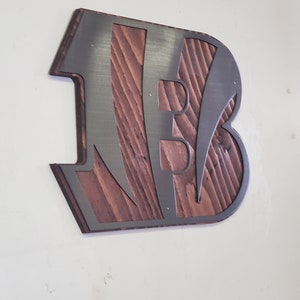 A steel angular emblem with diagonal stripe cutouts over rustic stained wood, angled on a light wall with a darker steel finish.