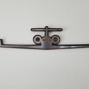 May include: A wooden and metal airplane-shaped wall decor piece. The design features a central airplane silhouette with wings extending horizontally. The metal is silver-colored, and the wood has a dark brown finish.