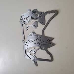 K&ouml;nnte beinhalten: Metallische Wandkunst mit der Umrissform des Bundesstaates Minnesota und zwei ausgeschnittenen Barschen. Die Fische sind in entgegengesetzte Richtungen gerichtet und befinden sich auf beiden Seiten der Staatsumrissform.