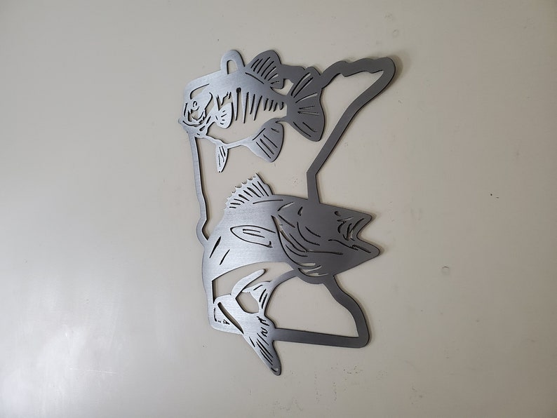 K&ouml;nnte beinhalten: Metallische Wandkunst mit der Umrissform des Bundesstaates Minnesota und zwei ausgeschnittenen Barschen. Die Fische sind in entgegengesetzte Richtungen gerichtet und befinden sich auf beiden Seiten der Staatsumrissform.