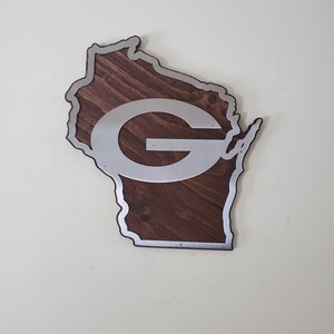 Close angled view of the curved wall decor with a steel emblem layered over dark brown stained wood and a silver border along the edge.