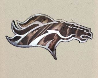 Puede incluir: Un letrero decorativo de pared con forma de perfil de cabeza de caballo. El diseño presenta un contorno y acentos interiores de color plata metálica que contrastan con una incrustación de textura de madera marrón oscuro en el cuerpo.