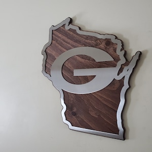Angled view of the map-style wall decor with a silver steel emblem and steel border over rustic stained wood grain, shown on a light gray background.