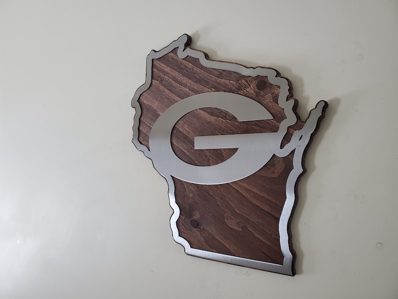 Angled view of the map-style wall decor with a silver steel emblem and steel border over rustic stained wood grain, shown on a light gray background.