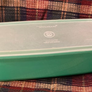 以下が含まれることがあります： 透明な蓋が付いた緑色の長方形のタッパーウェア容器。蓋には「タッパーウェア」と印刷されています。