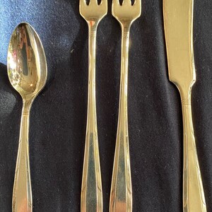 May include: Set of four gold-toned flatware pieces, including two forks, a butter knife, and a spoon.