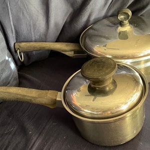 May include: Two stainless steel pots with lids and wooden handles. The pots are silver and have a shiny finish. The lids are also silver and have a shiny finish. The handles are brown and have a textured finish.